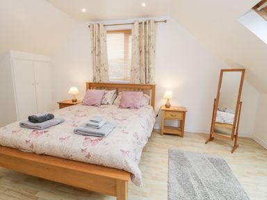 A bedroom with a wooden bed and nightstands with lamps a standing mirror a window with curtains and a rug on the floor at Ty Coch in Llanberis
