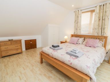 A bedroom with a wooden bed a dresser a wardrobe and a window with curtains at Ty Coch in Llanberis
