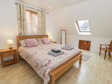 A bedroom with a wooden bed with pink and patterned bedding two side tables with lamps a window with curtains a skylight two folded towel sets a full-length mirror a wooden chair and a small rug at Ty Coch in Llanberis