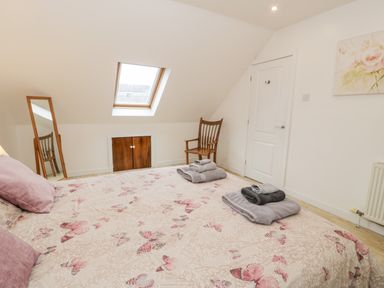 A bedroom with a bed covered in butterfly patterned bedding a wooden chair a full length mirror a skylight window and folded towels on the bed at Ty Coch in Llanberis