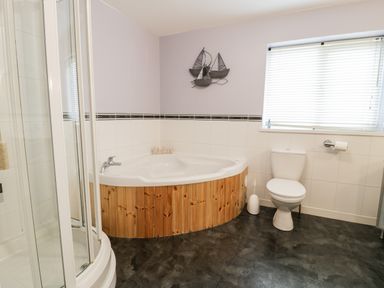 A bathroom with a corner bathtub with wood paneling a shower cubicle a toilet and a window with blinds at Ty Coch in Llanberis
