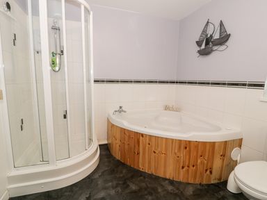 A bathroom with a corner shower, a corner bathtub with wooden paneling, and a toilet at Ty Coch in Llanberis