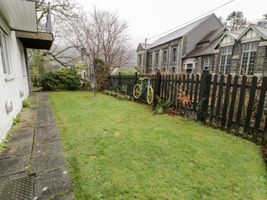 A backyard with grass a paved pathway a black picket fence and a bicycle hanging on the fence at Ty Coch in Llanberis