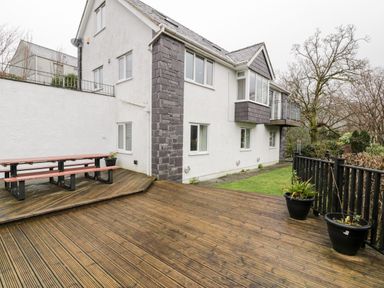 An outdoor wooden deck with a picnic table and two large plant pots beside a white house at Ty Coch in Llanberis