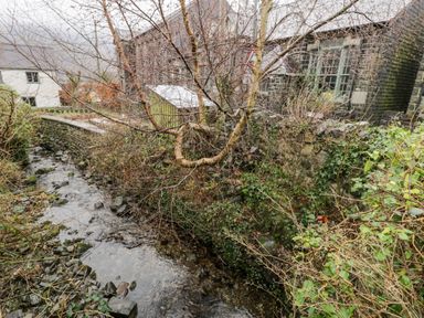 A small stream running beside stone houses with leafless trees and greenery at Ty Coch in Llanberis