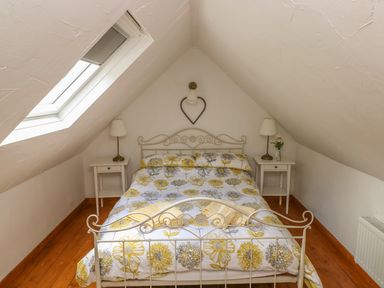 A bedroom with a double bed with floral bedding two bedside tables with lamps and a skylight window at Snowdrop Cottage in Laugharne