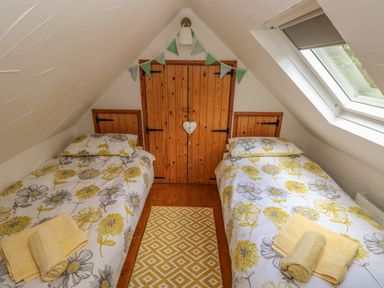 A small attic bedroom with two single beds opposite each other with floral bedding and yellow towels on a wooden floor with a window on the right at Snowdrop Cottage in Laugharne