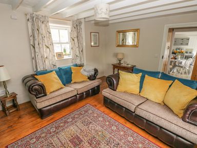 A living room with two sofas with yellow and blue cushions a wooden floor and a patterned rug at Snowdrop Cottage in Laugharne