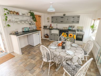 A kitchen with a round table set with plates and sunflowers in a vase at Snowdrop Cottage in Laugharne