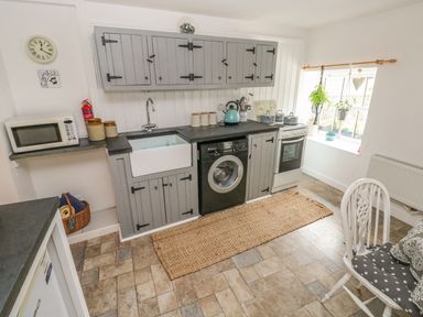 A kitchen with gray cabinets a washing machine a oven and a microwave at Snowdrop Cottage in Laugharne