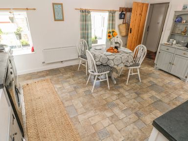 A kitchen with a round dining table set with croissants and chairs near windows with curtains at Snowdrop Cottage in Laugharne