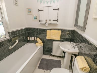 A bathroom with a bathtub sink and toilet with yellow towels and dark tiled walls at Snowdrop Cottage in Laugharne