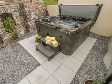 An outdoor hot tub with two steps a pair of yellow towels and two glasses near a stone wall at Snowdrop Cottage in Laugharne