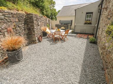An outdoor patio area with a dining table and chairs on gravel next to stone walls and a hot tub at Snowdrop Cottage in Laugharne