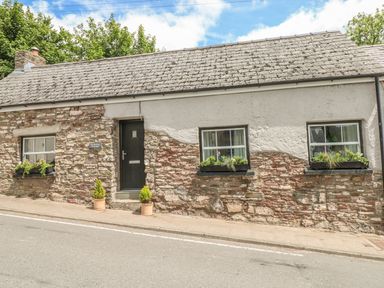 A single story stone cottage with three windows and a black door with potted plants outside at Snowdrop Cottage in Laugharne