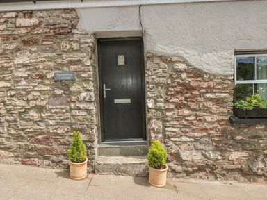 A stone cottage entrance with a black door two potted plants and a window with a planter box at Snowdrop Cottage in Laugharne