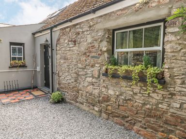 A cobblestone courtyard with a stone wall and window with plants at Snowdrop Cottage in Laugharne