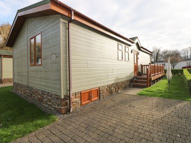 An exterior view of a single-story building with a wooden porch and paved pathway at The Retreat in Wisemans Bridge near Saundersfoot