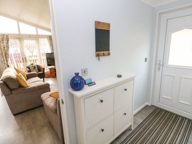 A hallway with a white cabinet next to a white door and a living room with sofas and a TV in the background at The Retreat in Wisemans Bridge near Saundersfoot