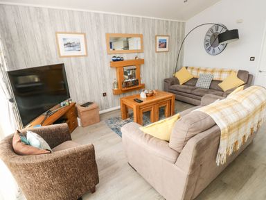 A living room with sofas armchair coffee table television and wall clock at The Retreat in Wisemans Bridge near Saundersfoot