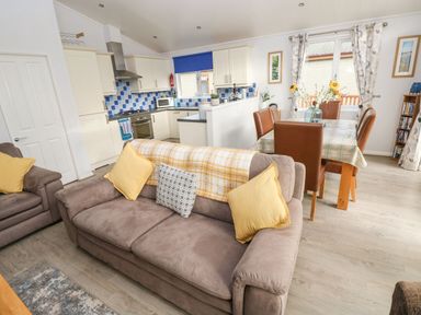 An open plan living area with brown sofas yellow cushions a dining table with brown chairs and a kitchen with white cabinets and blue tiled backsplash at The Retreat in Wisemans Bridge near Saundersfoot