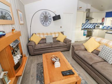 A living room with two sofas a wooden coffee table a fireplace and a kitchen area with white cabinets and a blue tiled backsplash at The Retreat in Wisemans Bridge near Saundersfoot