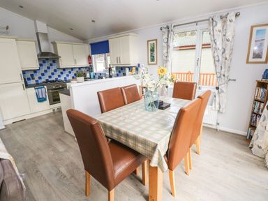 A dining area with a table covered with a checkered cloth and six brown chairs next to a kitchen with blue tiled backsplash at The Retreat in Wisemans Bridge near Saundersfoot