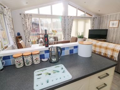 A kitchen counter with a kettle and canisters overlooking a dining area with chairs and a living room with a sofa and TV at The Retreat Wisemans Bridge near Saundersfoot