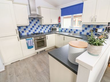 A kitchen with white cabinets blue tiled backsplash and a countertop with a plant and container at The Retreat Wisemans Bridge near Saundersfoot