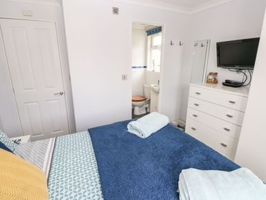 A bedroom with a bed covered in blue blankets and towels a white dresser with a TV mounted on the wall and a door leading to a bathroom at The Retreat Wisemans Bridge near Saundersfoot