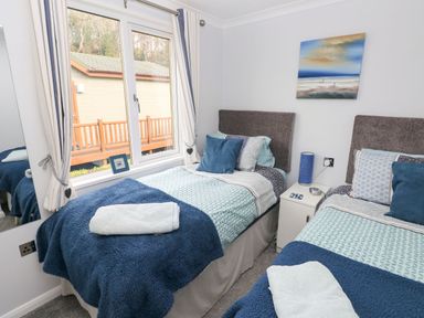 A bedroom with two single beds blue blankets and pillows a window and a painting at The Retreat in Wisemans Bridge near Saundersfoot