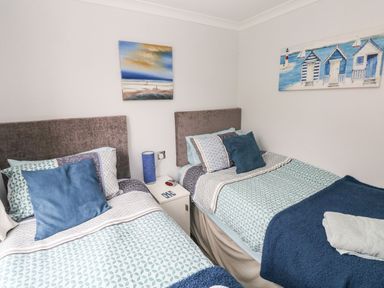 A bedroom with two single beds a small white nightstand between them and paintings on the walls at The Retreat in Wisemans Bridge near Saundersfoot