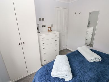 A bedroom with a blue bedspread and two white towels on the bed a white wardrobe and chest of drawers a wall mirror and a closed door at The Retreat Wisemans Bridge near Saundersfoot