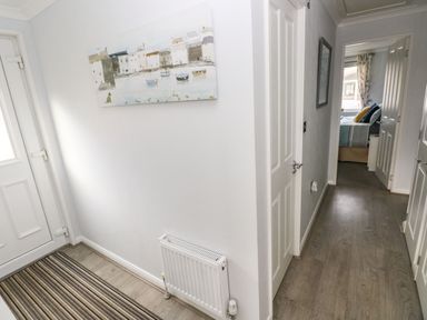 A hallway with a striped rug a white radiator a painting on the wall and doors leading to a bedroom at The Retreat in Wisemans Bridge near Saundersfoot