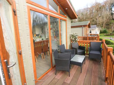 A wooden deck with four black wicker chairs and a glass table outside a house with large windows at The Retreat in Wisemans Bridge near Saundersfoot