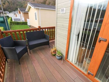 A wooden deck with two black chairs and potted plants outside a building at The Retreat Wisemans Bridge near Saundersfoot
