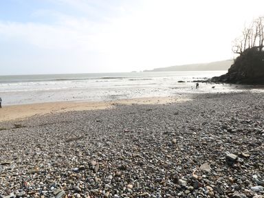 A pebble and sand beach with a person and dog near the water at The Retreat in Wisemans Bridge near Saundersfoot