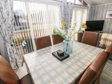 A dining table with a checkered tablecloth and flower vase in a room with leather chairs and sliding glass doors at The Retreat in Wisemans Bridge near Saundersfoot