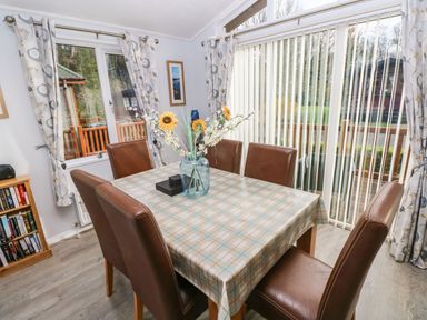 A dining room with a table covered by a checkered tablecloth six brown chairs flowers in a vase and windows with patterned curtains at The Retreat Wisemans Bridge near Saundersfoot