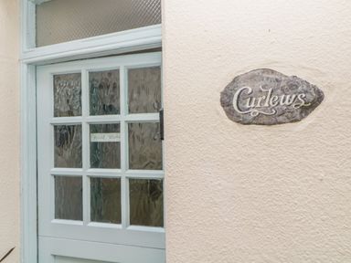 A door with glass panels and a sign reading Curlews on the wall at Curlews Cottage in Looe