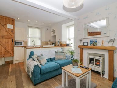A living room with a blue sofa, a small wooden table, and a fireplace at Curlews Cottage in Looe