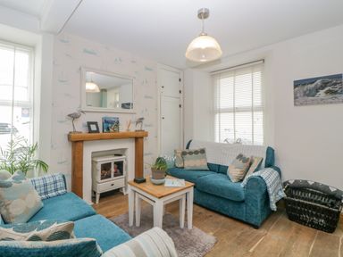 A living room with two blue sofas a small wooden coffee table a fireplace with a wooden mantel and a large mirror above it at Curlews Cottage in Looe