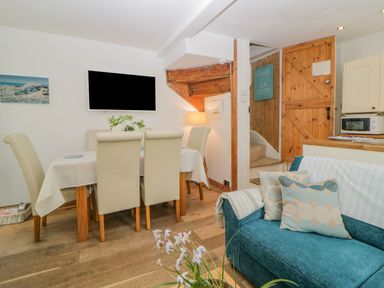 A dining area with beige chairs and a table with a white tablecloth next to a blue sofa with cushions and a wooden door at Curlews Cottage in Looe