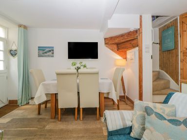A dining area with a table and six chairs a wall-mounted TV and a corner with stairs at Curlews Cottage in Looe