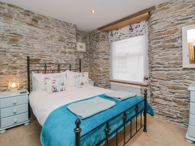 A bedroom with a bed with blue blanket and two towels on it stone walls and two blue bedside drawers at Curlews Cottage in Looe