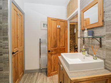 A bathroom with a wooden door open to a hallway a sink with mirror and shelf and a towel radiator at Curlews Cottage in Looe