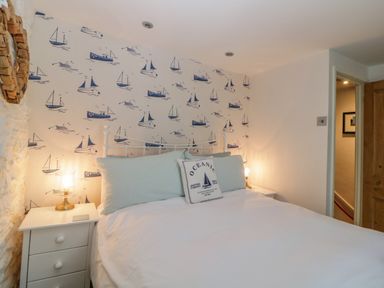 A bedroom with a white bed and nautical-themed wallpaper at Curlews Cottage in Looe