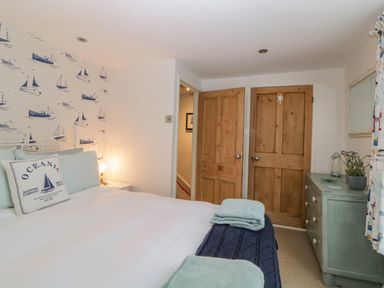 A bedroom with a bed towels wooden doors a green dresser and wallpaper with boats at Curlews Cottage in Looe