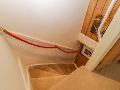 A carpeted spiral staircase with a red rope handrail and wooden wall paneling at Curlews Cottage in Looe