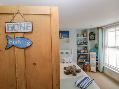 A bedroom with a single bed a stuffed turtle on the bed shelves with books and games and a window with blinds at Curlews Cottage in Looe